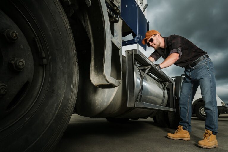 Truck driver inspecting a semi-truck fuel tank and tires under cloudy sky, representing truck driver duties and responsibilities.